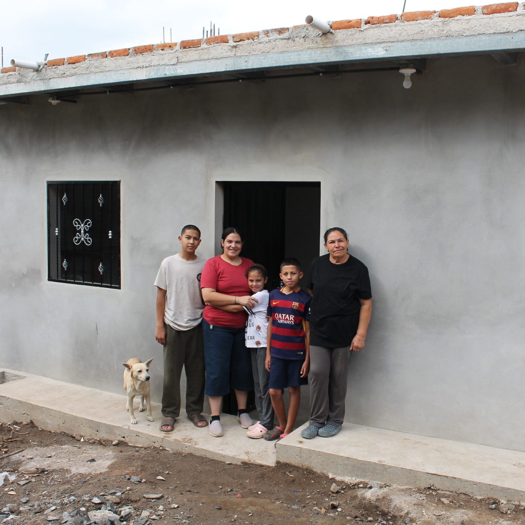 A family of five smiles for the camera while standing in front of a doorway of a building