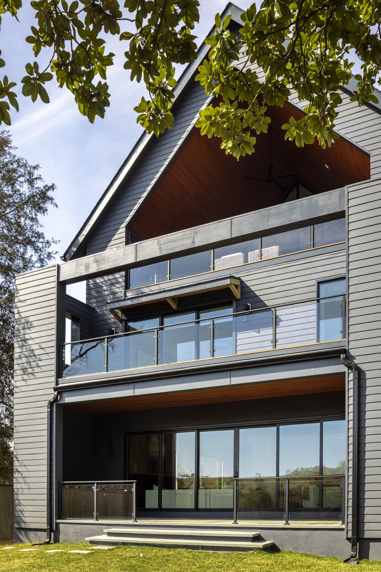 A ground-level view of the back of a modern-built home with a tall pointed roof