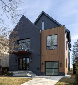 A modern-looking black-and-brown house with a driveway leading up to the garage