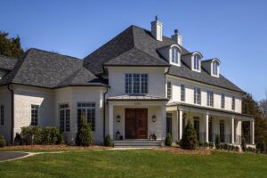 A front facing view of a white brick house with a black slatted roof