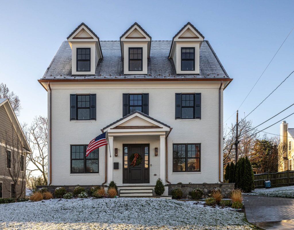 A white house with an American flag flying in front of the front door. The house and lawn is covered in fresh-fallen snow