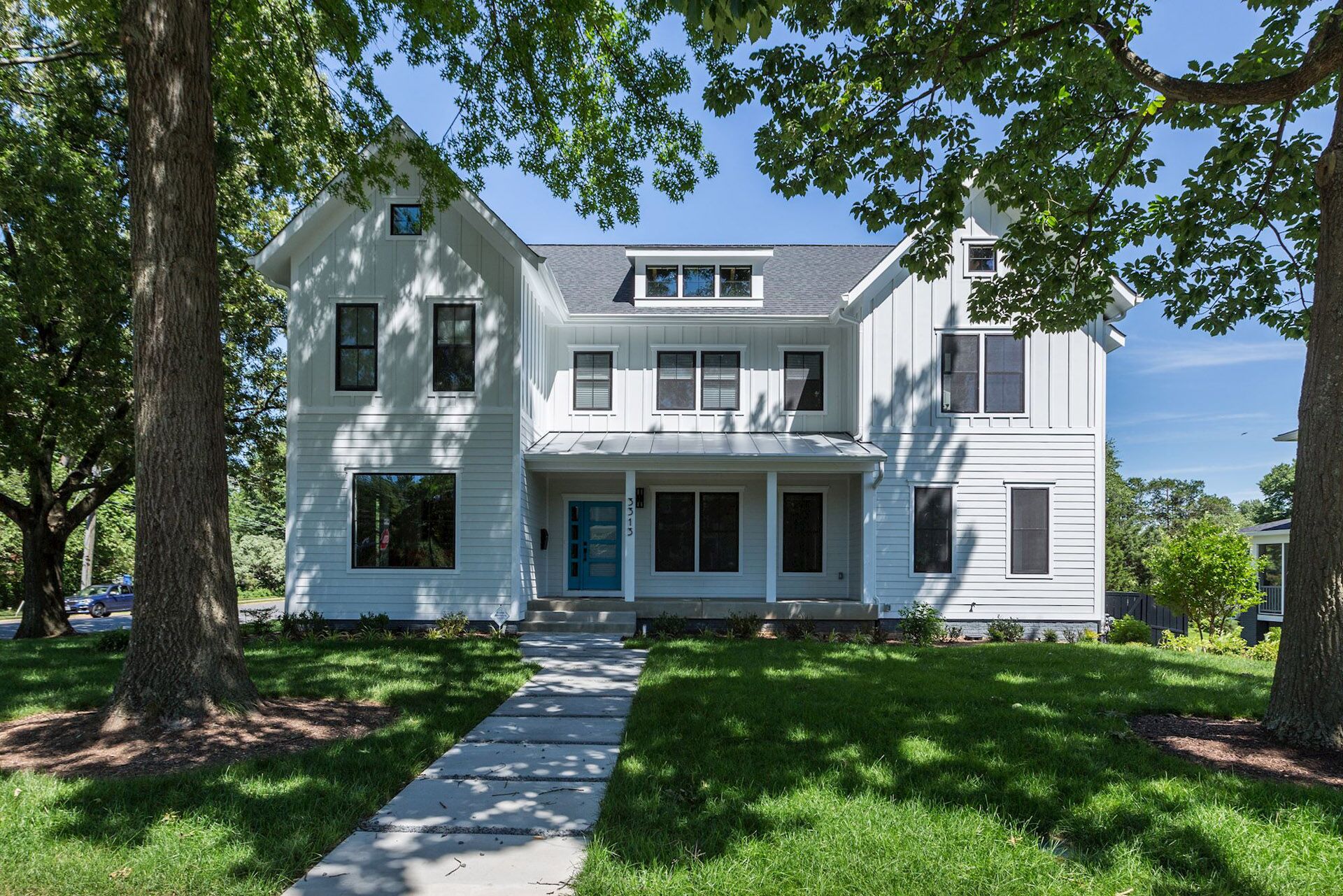 A white house shaded by two large leafy trees, with a pavers walkway leading up to the front door