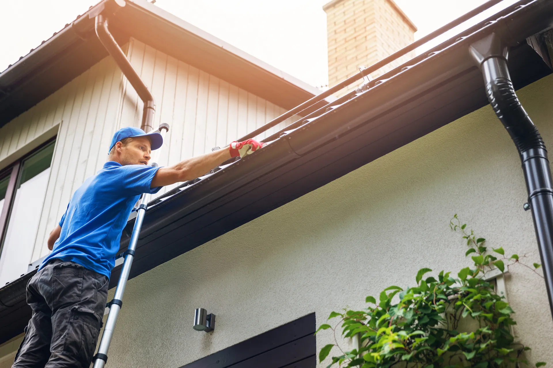 A man standing on a ladder cleaning his gutters.