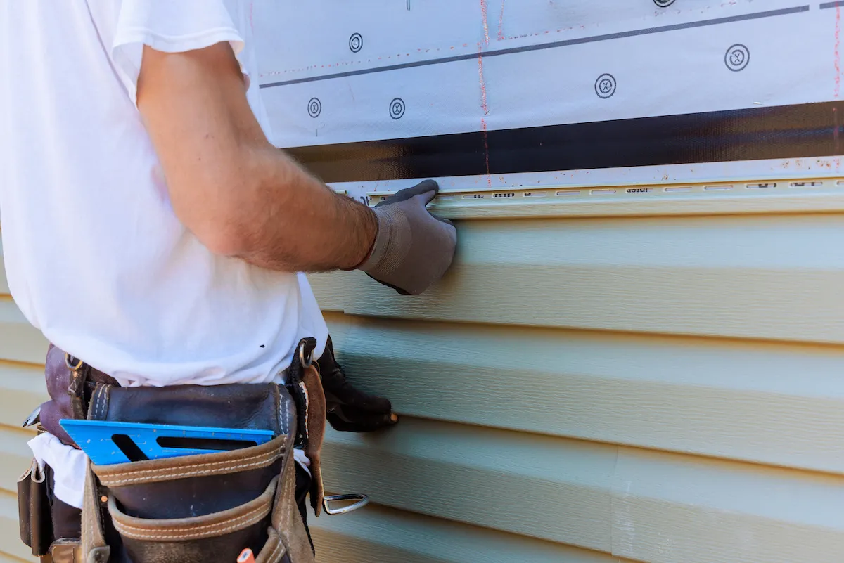 A construction worker installing siding on the side of a house.